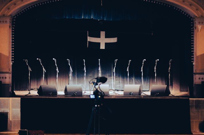 A row of microphones on an empty stage with a Cornish flag behind