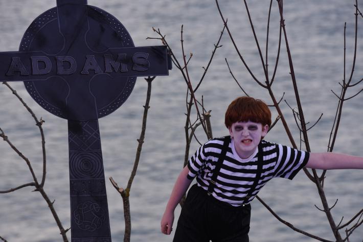 A ghoulish child snarls next to a large tombstone marked Addams