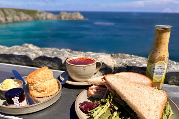 Plates of food, scones with jam and cream, a sandwich, bottle of sauce and a cup of coffee on balcony overlooking the sea