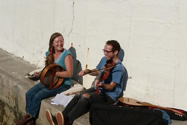 Bec Applebee and Richard Trethewey playing instruments on a seawall