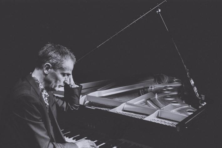 Moody black and white image of Simon Latarche at his grand piano