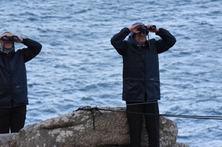 Two actors in raincoats looking through binoculars